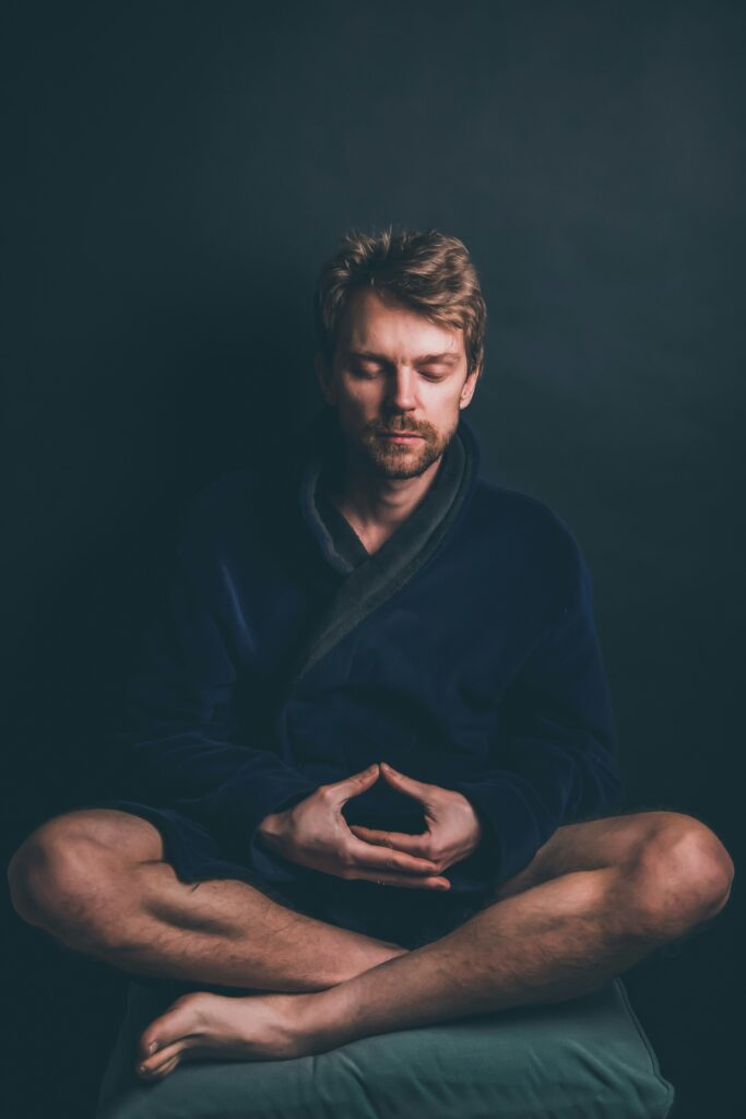 a man meditating on his own, sitting on the ground with the hands over his knees